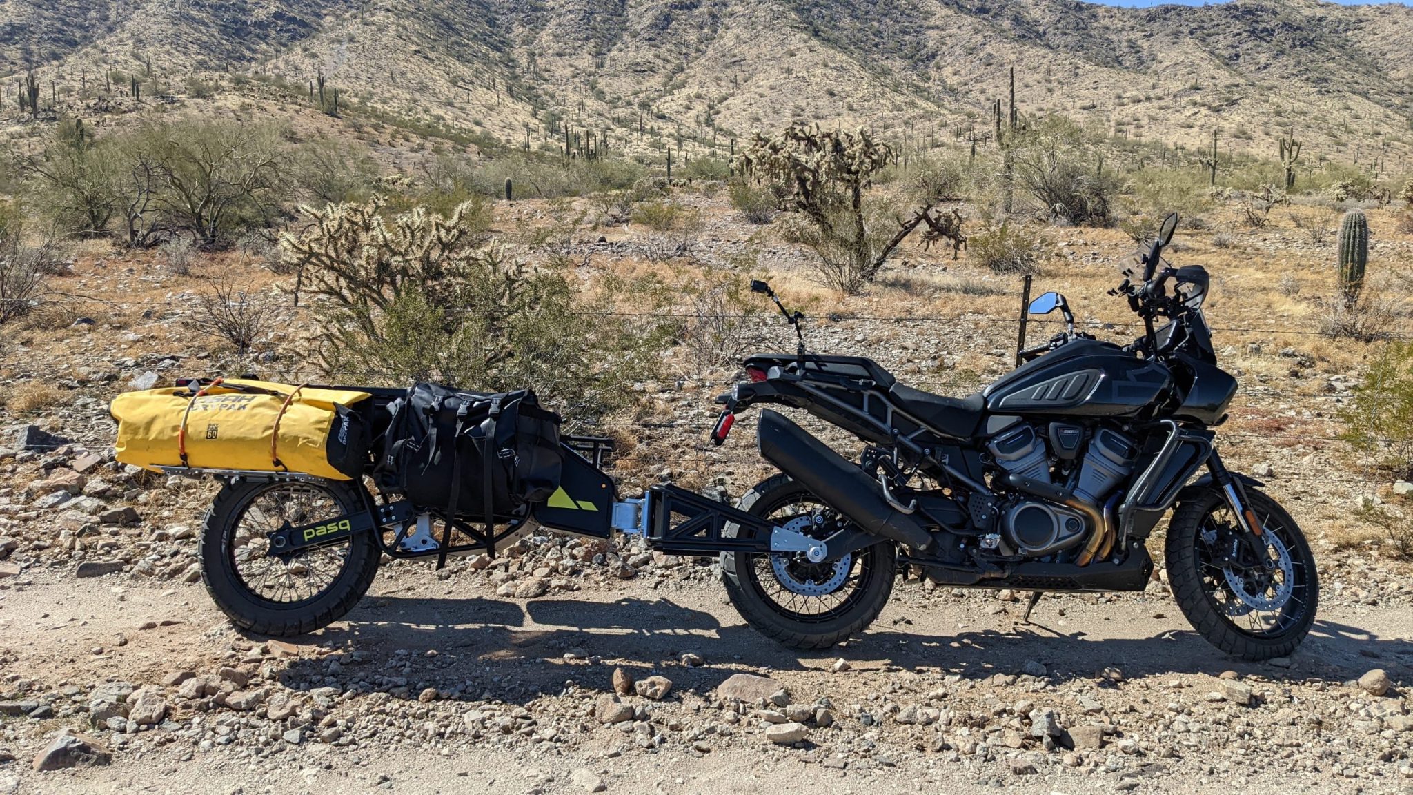 THe ADV1 trailer connected to a bike parked in the Arizona desert. The ADV1 has a yellow duffel bag and a black soft bag attached to the front side. End ID.